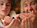 A woman and a child smile while handling small black bugs.