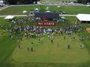 Drone aerial shot of Lake Wheeler Turf Field Lab, pavilion and turf painted "NC State" during 2022 Turfgrass Field Day. Attendees are clustered around the pavilion listening to announcements.