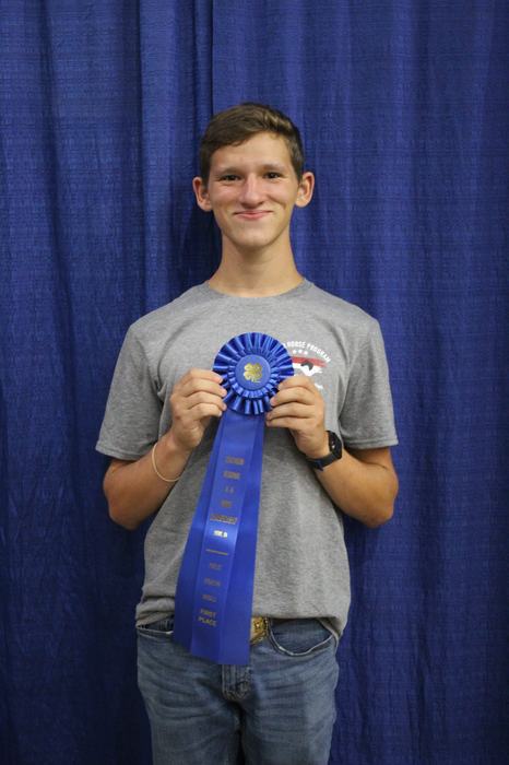 Young man holding a blue ribbon reading "First Place" against a blue curtain