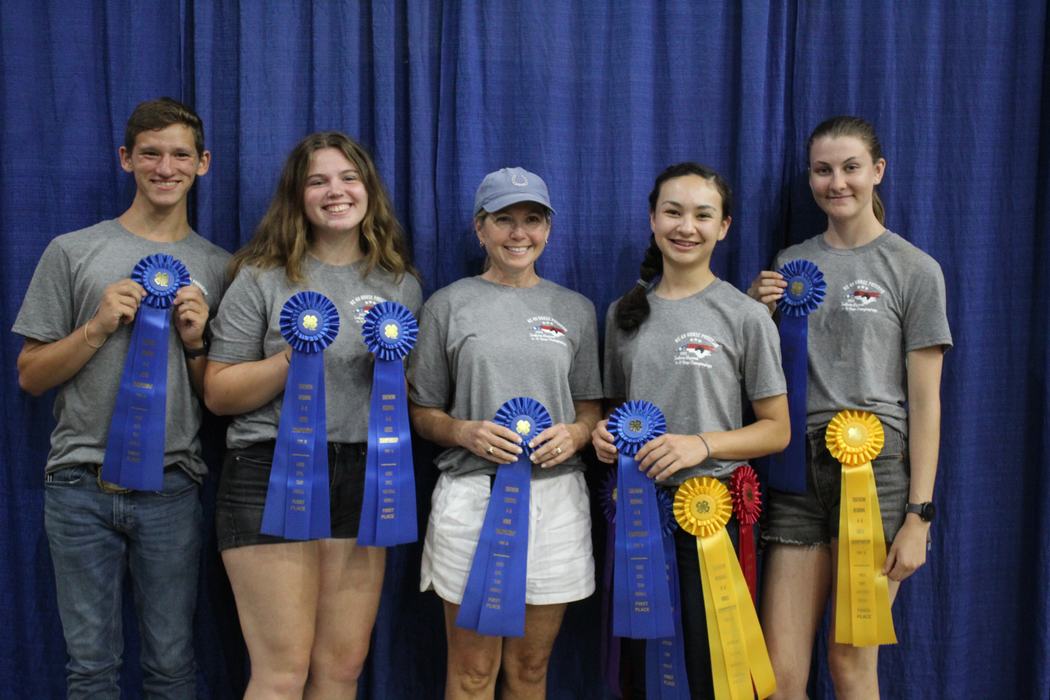 Five people standing before a blue curtain holding ribbons that say "First Place."