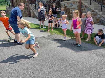 Group of children racing and watching outside a stone building with door labeled "MEN".
