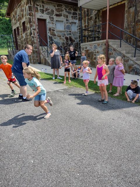 Group of children racing and watching outside a stone building with door labeled "MEN".