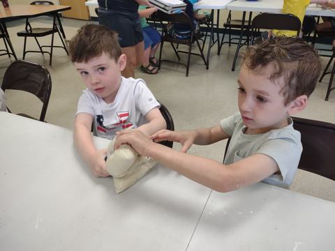 Two young boys seated at a table squeezing a plastic bag of dough