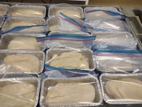 Rows of aluminum loaf pans with dough covered by Ziploc bags