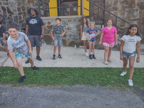 Children and adult standing by a stone wall on a sidewalk; boy's shirt reads "DARE."