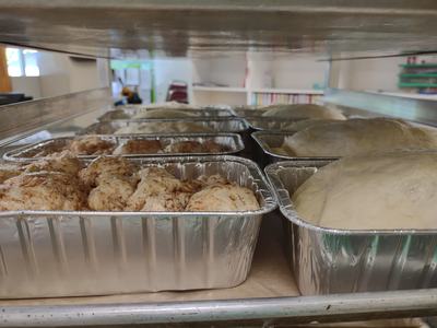 Aluminum pans with risen dough and cinnamon-topped rolls on a bakery rack