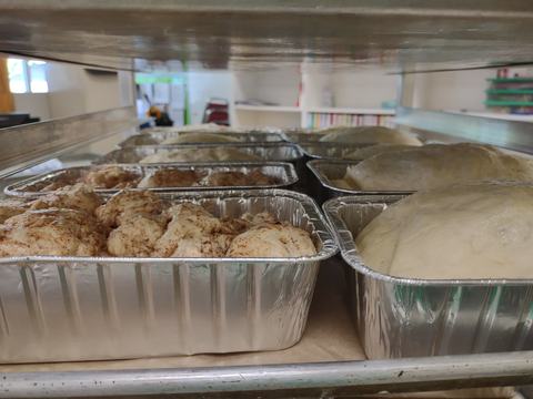 Aluminum pans with risen dough and cinnamon-topped rolls on a bakery rack
