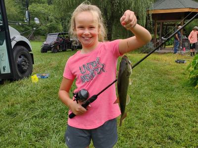 Young girl holding a fishing rod with a caught fish, wearing pink shirt reading UNDER ARMOUR