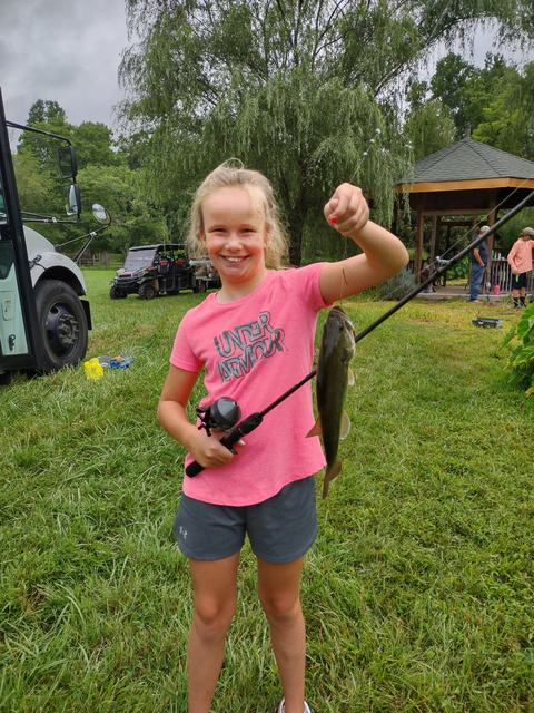 Young girl holding a fishing rod with a caught fish, wearing pink shirt reading UNDER ARMOUR