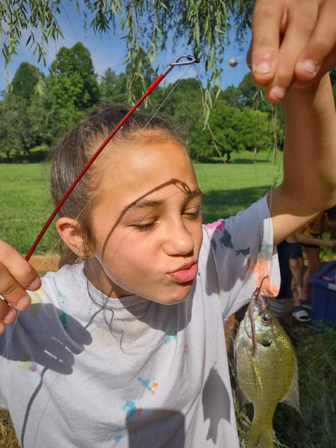 Girl holding fishing pole with hooked sunfish near her face