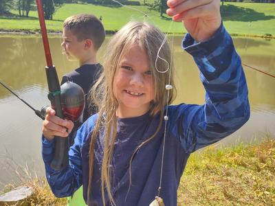Child holding fishing rod and line with a caught sunfish by a pond