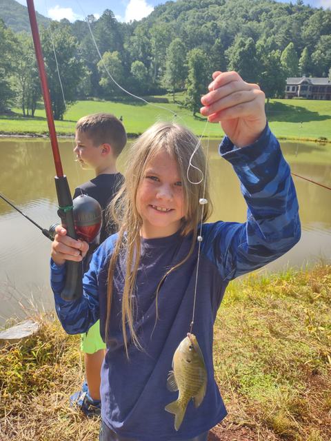 Child holding fishing rod and line with a caught sunfish by a pond