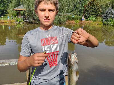 Young boy on dock holding fishing rod and a bass; shirt reads "ATTACK THE RIM"