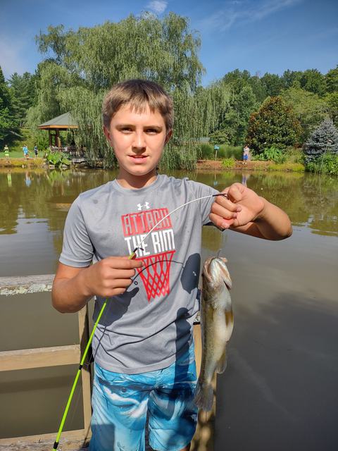 Young boy on dock holding fishing rod and a bass; shirt reads "ATTACK THE RIM"