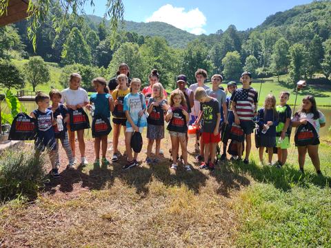 Group of children standing by a pond with fishing rods and North Carolina National Guard bags