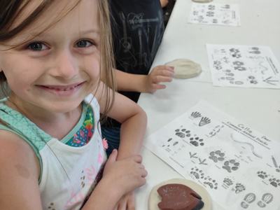 Young girl at table with clay impression and animal track guide, other children seated nearby