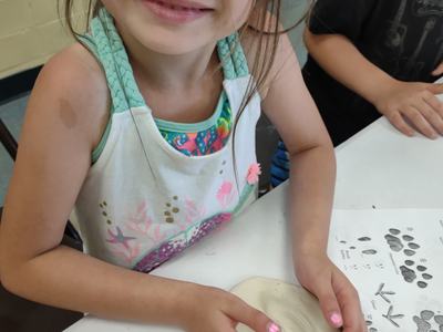 Child shaping a clay disk with hands at a table, animal-track printout beside them