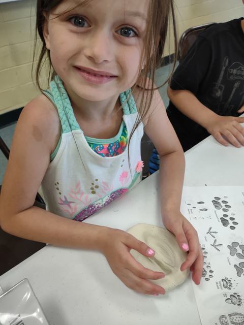 Child shaping a clay disk with hands at a table, animal-track printout beside them