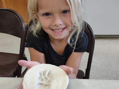 Child holding a round clay plaque with an animal paw print impression