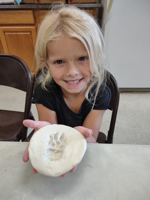 Child holding a round clay plaque with an animal paw print impression