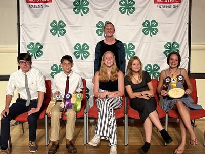 Six youth seated with ribbons and a plaque in front of NC State Extension 4-H backdrop