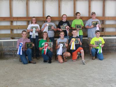 Children in a barn posing with appreciation plaques and ribbons.