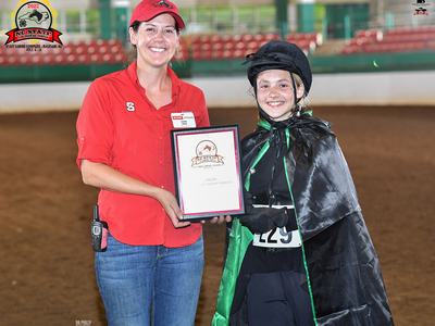 Woman in red presents NC State award plaque to young rider in helmet and black cape