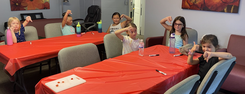 Children seated at red-covered tables showing thumbs up or thumbs down