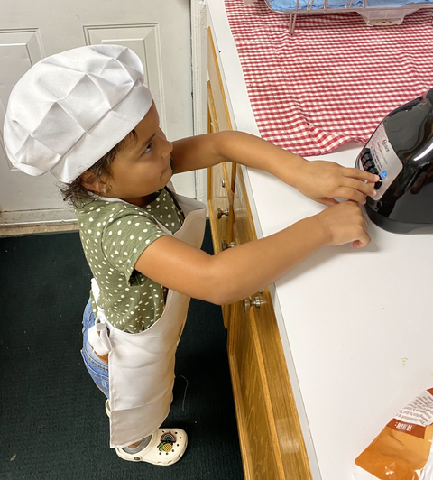 Toddler in chef hat and apron pressing buttons on a countertop blender