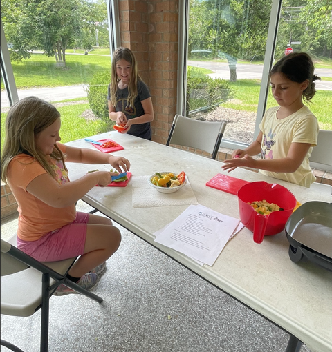 Three girls at a table chopping and preparing vegetables with cutting boards and bowls
