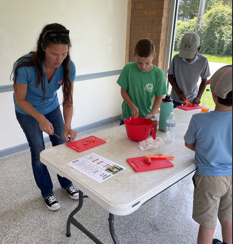 Adult and three children cutting vegetables at a table with red cutting boards