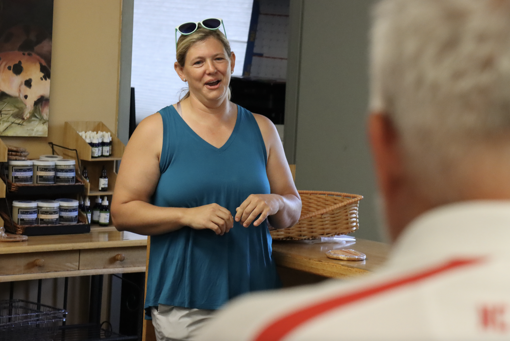A woman in a green shirt and sunglasses speaks to a person.