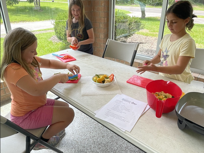 Three girls at a table chopping and preparing vegetables with cutting boards and bowls