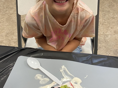 Young girl seated behind a watermelon slice topped with yogurt, diced kiwi, and blueberries