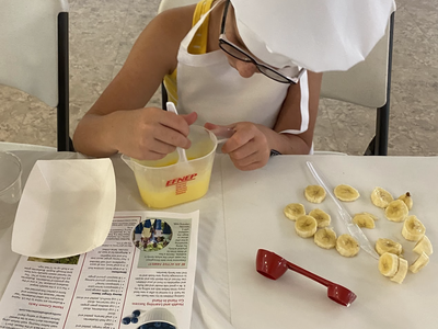 Child in chef hat stirring yellow mixture, EFNEP container and "Harvest of the Month" leaflet
