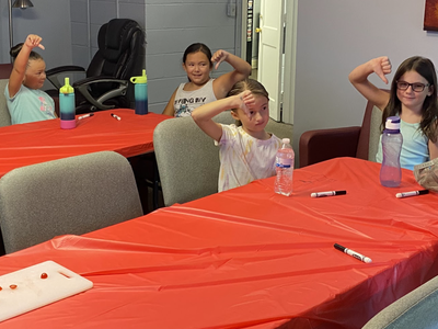 Children seated at red-covered tables showing thumbs up or thumbs down