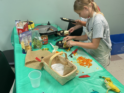 Girl assembling wraps at table with chopped bell peppers, jarred salsa, and utensils