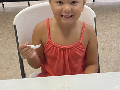 Girl in red dress holding a spoon, yogurt-covered watermelon slice topped with blueberries.