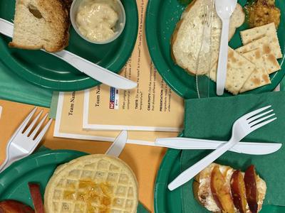 Four green paper plates with toast, waffle, crackers, peach slices and plastic utensils