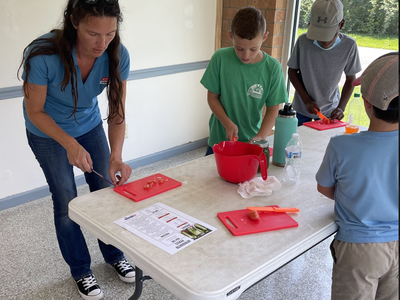 Adult and three children cutting vegetables at a table with red cutting boards