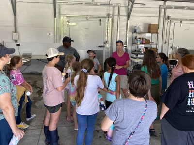 Children and adults in a metal garage listening to a woman speaking
