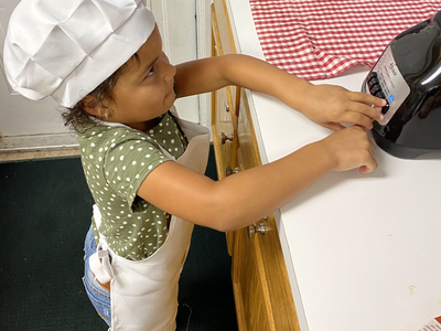 Toddler in chef hat and apron pressing buttons on a countertop blender