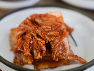 Fermented spicy kimchi (napa cabbage) piled on a white-rimmed plate