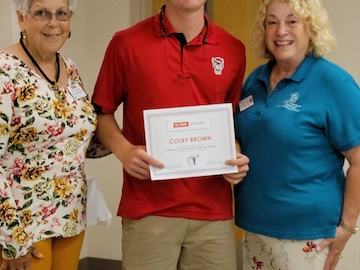 Young man holding certificate reading "COLBY BROWN" standing between two older women