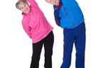 Two seniors performing standing side bends, woman in pink sweater and man in blue jacket