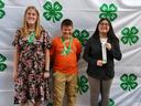 Three youths stand in front a 4-H banner and display their awards.