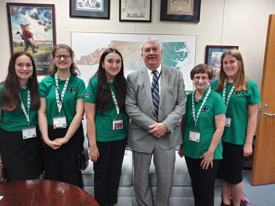 Youths and adults in green 4-H shirts stand in front of a map of the state of North Carolina.