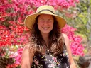 Woman wearing straw hat and floral dress standing in front of pink azalea bushes