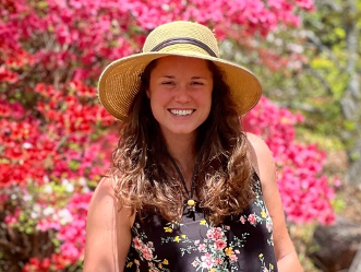 Woman wearing straw hat and floral dress standing in front of pink azalea bushes