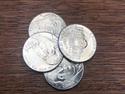 Four U.S. nickels showing Monticello and "IN GOD WE TRUST" on a wood table.